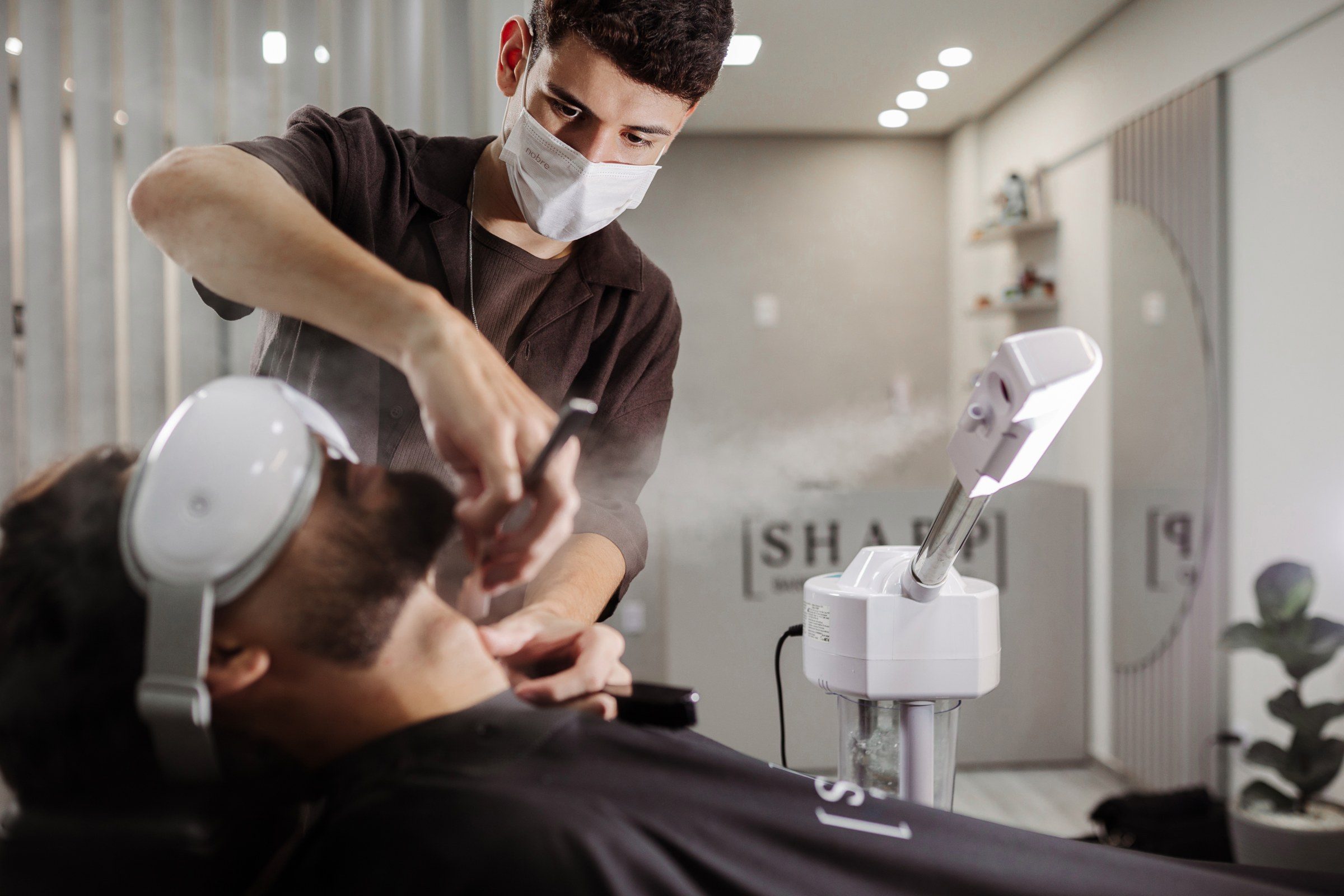 Barba sendo feita na navalha com vaporizador facial ligado ao lado