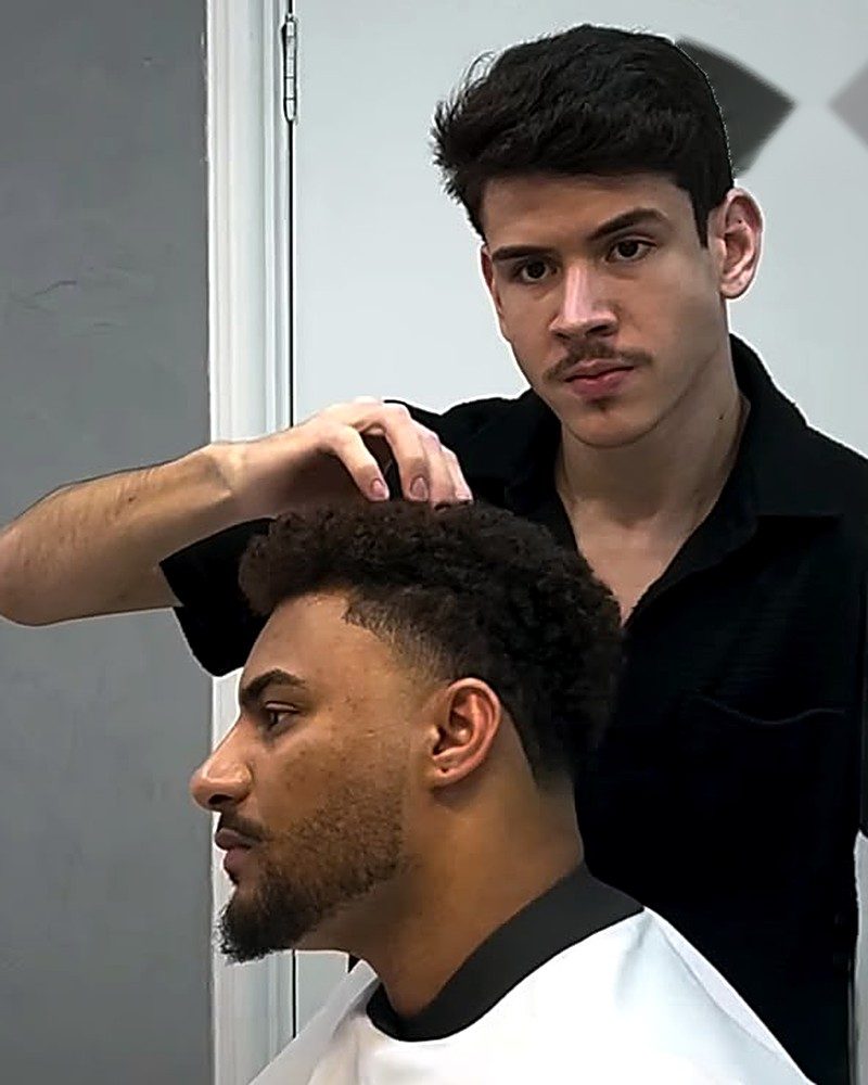 Gabriel finalizando corte com topo cacheado e degradê nas laterais
