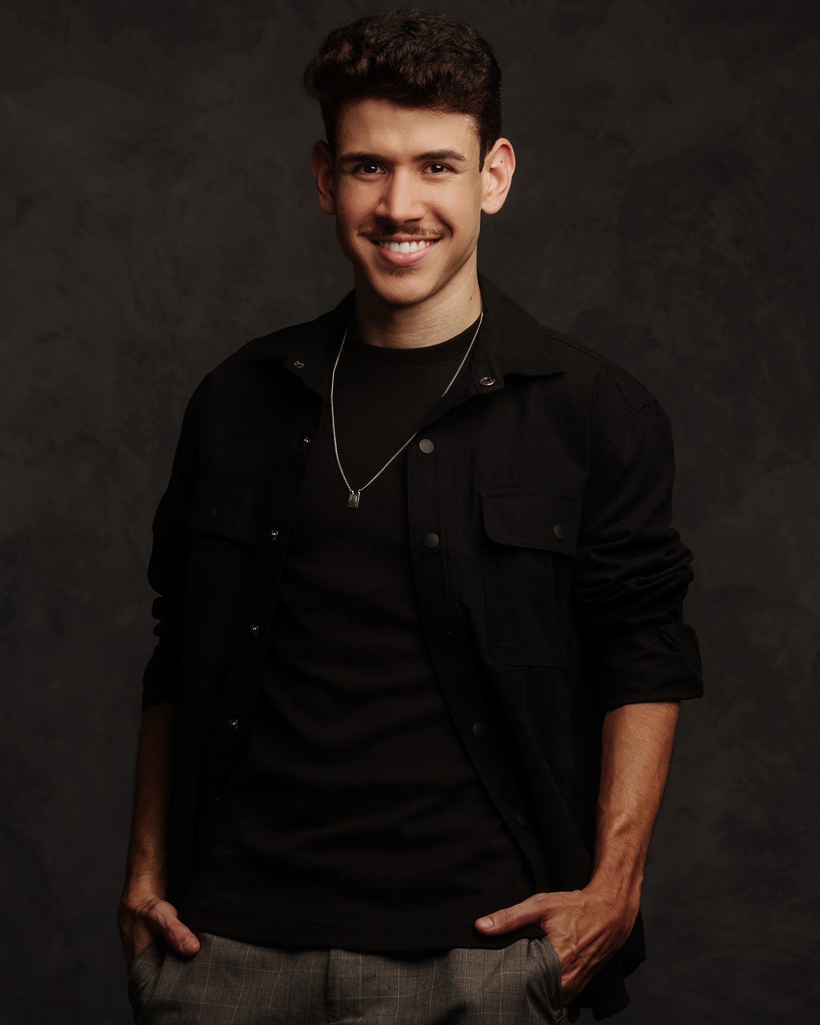 Gabriel sorrindo, de camisa escura, em fundo escuro