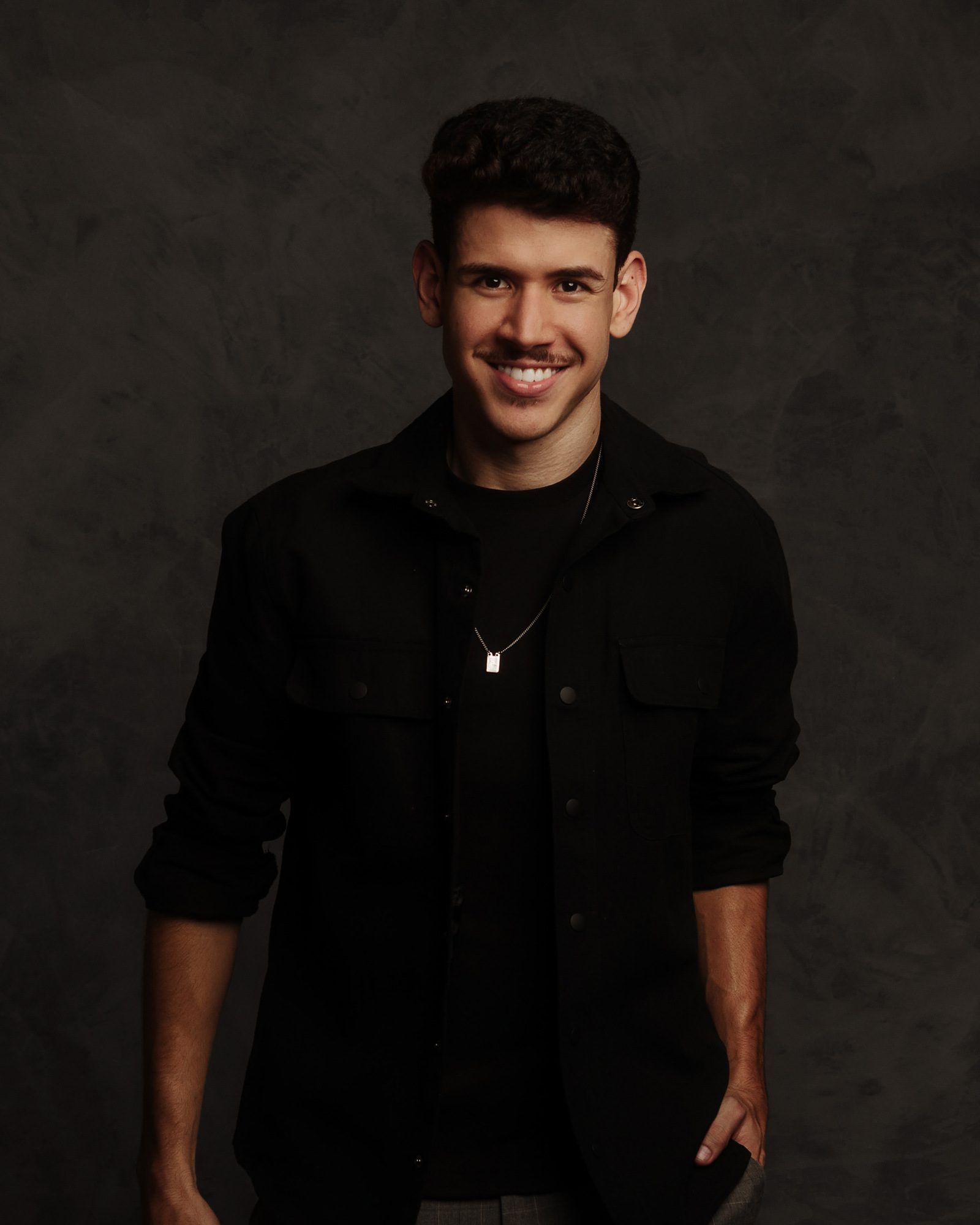 Gabriel Araújo, visagista da SHARP, sorrindo em fundo escuro